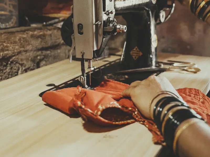 A hand guiding orange fabric under a sewing machine